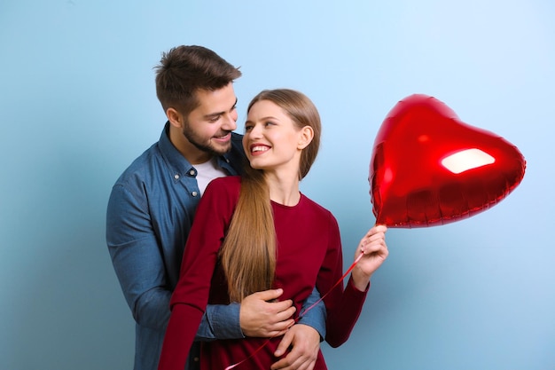 Linda pareja joven con globo en forma de corazón sobre fondo de color