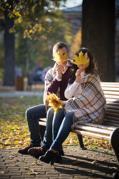 Una linda pareja joven sentada en el banco en el parque de otoño