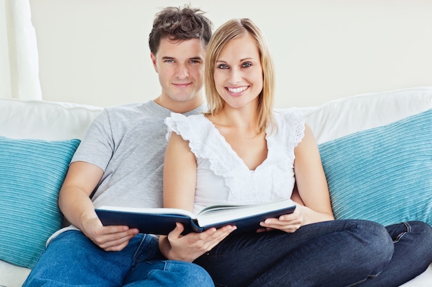 Linda pareja leyendo un libro juntos sentados en el sofá en casa