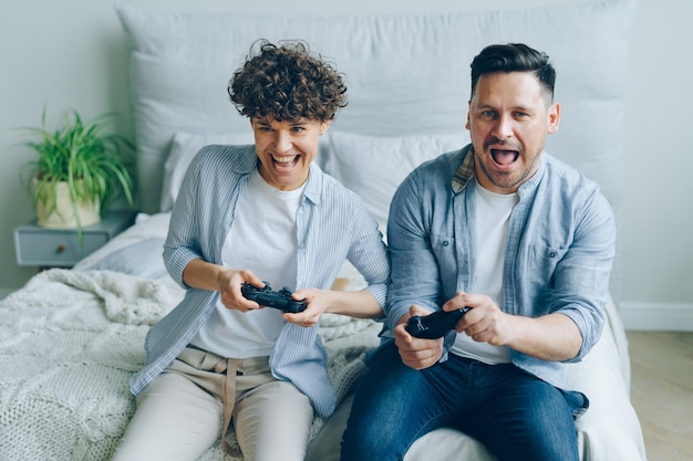 Foto linda pareja novio y novia jugando videojuegos sentados en la cama en el dormitorio