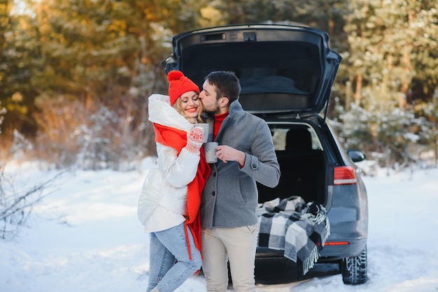 Linda pareja con picnic en el bosque de invierno bebiendo té de la taza de té para llevar. Picnic en la naturaleza. Cita de historia de amor en el coche.