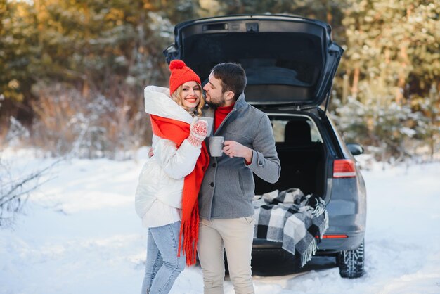 Linda pareja con picnic en el bosque de invierno bebiendo té de la taza de té para llevar. Picnic en la naturaleza. Cita de historia de amor en el coche.