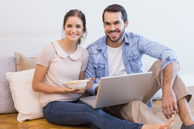 Linda pareja sentada en el piso usando laptop