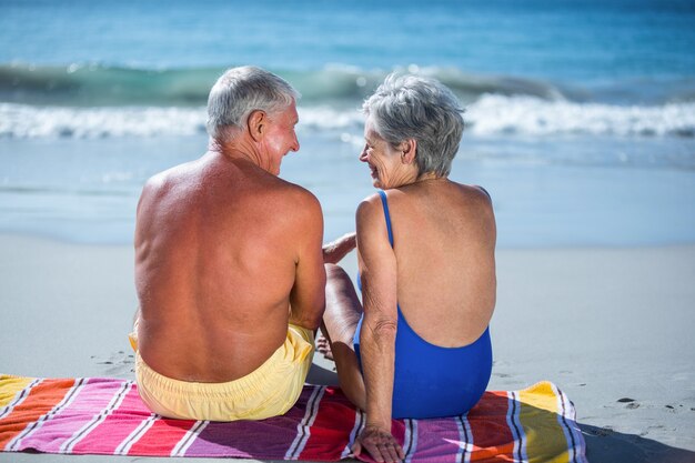 Linda pareja sentada en una toalla en la playa