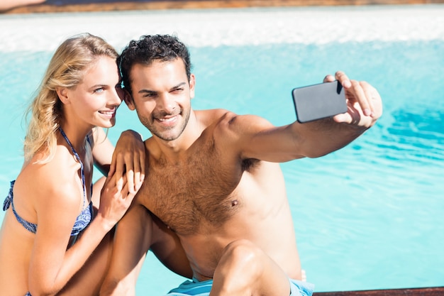 Linda pareja tomando selfie en la piscina