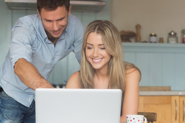 Linda pareja usando laptop juntos en casa en la cocina