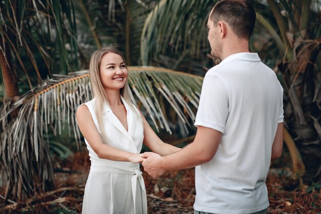 Linda pareja vestida de blanco tomados de la mano en una playa exótica sonriendo, palmas; concepto de sentimientos.