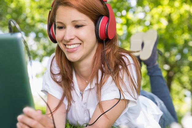 Linda pelirroja usando su tablet pc mientras escucha música en el parque