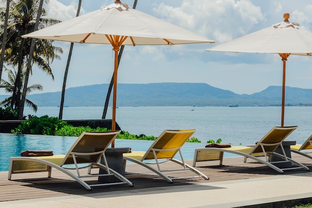 Foto linda piscina tropical no hotel ou resort com guarda-chuva cocos árvore espreguiçadeiras palmeiras com piscina infinita vista oceano e fundo de montanha