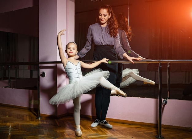 Linda professora de balé assistindo bailarina em bela pose durante a aula de dança Uma garotinha e seu instrutor estão envolvidos na coreografia na escola de balé