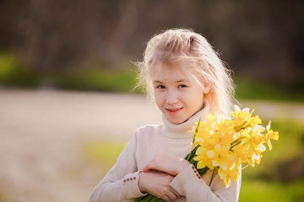 Linda rubia feliz niña con narcisos amarillos en el país de la primavera