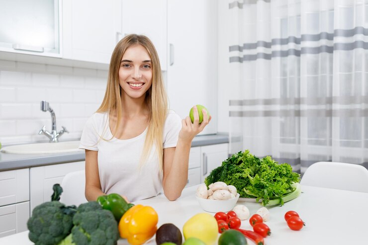 Linda rubia sosteniendo una manzana sentada en una mesa de cocina