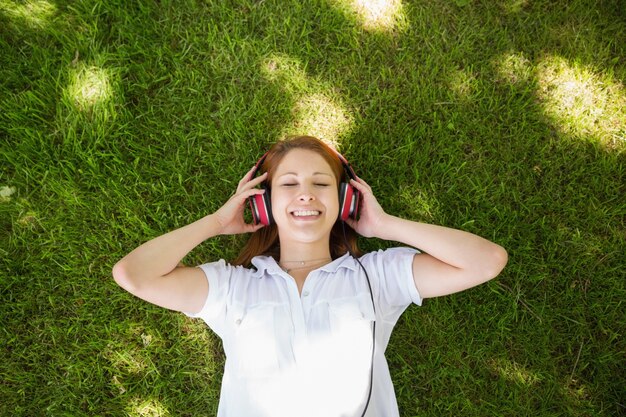 Linda ruiva deitada na grama, ouvindo música