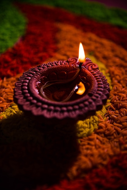 Linda saudação de Diwali usando Diya ou lâmpada de óleo de argila acesa e disposta sobre Rangoli feita por grãos de arroz multicoloridos, foco seletivo