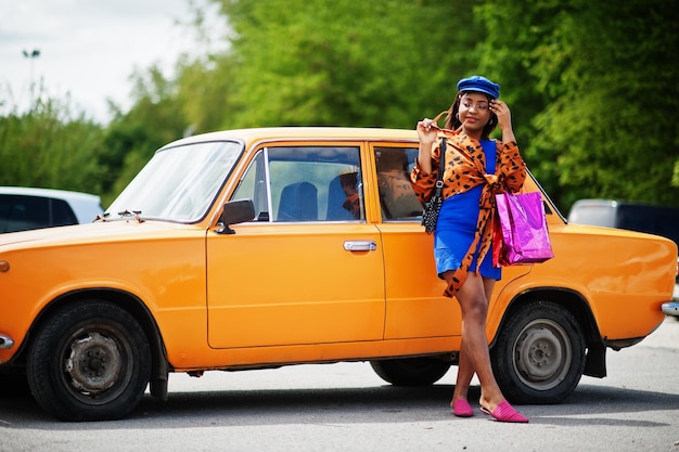 Linda senhora afro-americana com sacos de compras em pé perto de carro retrô clássico laranja