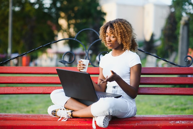 Linda senhora afro-americana com um computador no parque