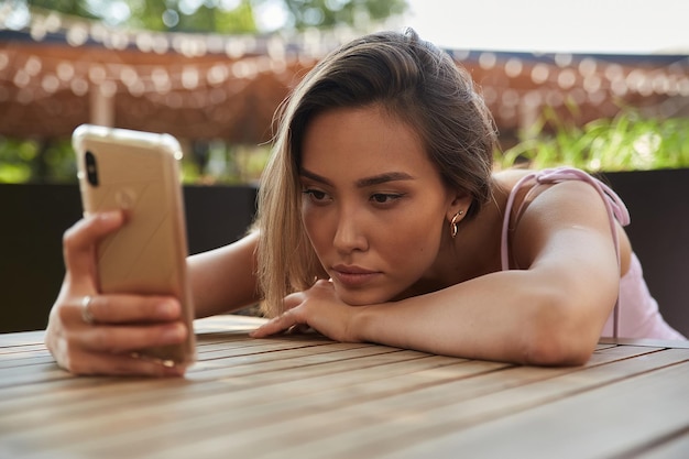 Linda senhora asiática melancólica pensativa deitada no café usando smartphone