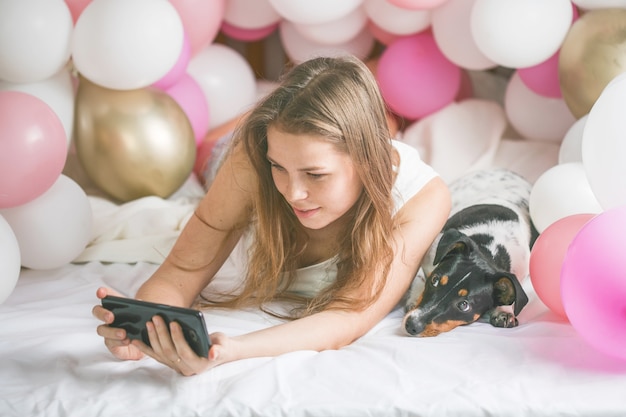 Linda senhora de pijama fazendo selfie no quarto dela usando o telefone e abraçar o cachorro dela.