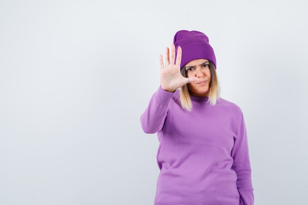 Linda senhora de suéter, gorro mostrando gesto de recusa e parecendo entediado, vista frontal.