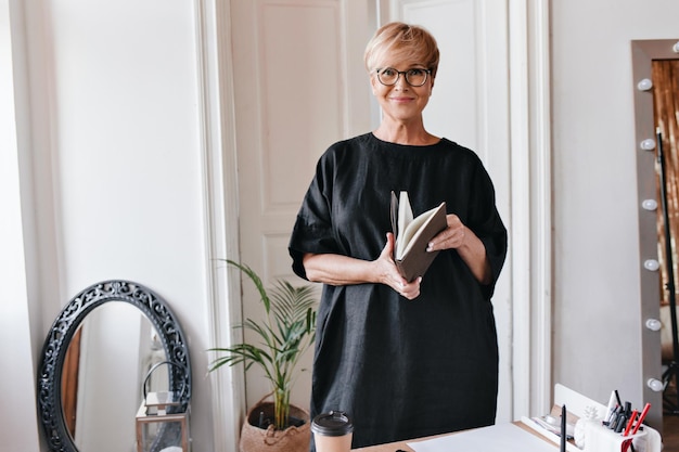 Linda senhora de vestido de grandes dimensões olha para a câmera e segura o notebook