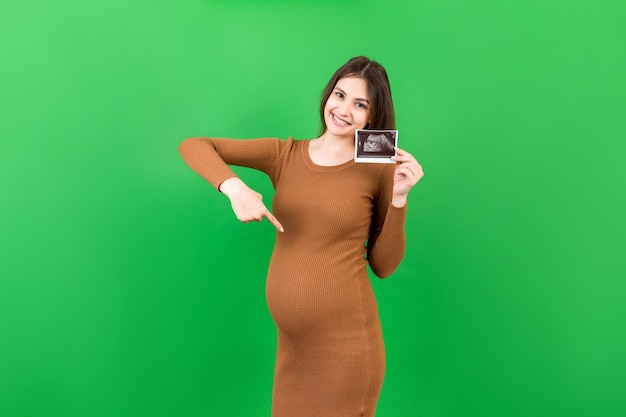 Linda senhora grávida posando com foto de sonografia de bebê perto de fundo colorido Conceito de gravidez ginecologia teste médico saúde materna