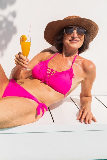 Linda senhora idosa tomando banho de sol e relaxando em uma piscina privativa durante o verão