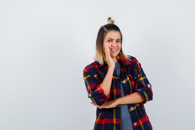 Linda senhora inclinando a bochecha por lado em camisa xadrez e parecendo feliz.