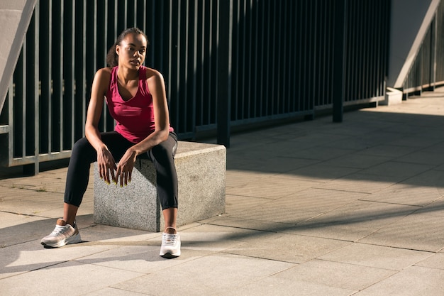 Linda senhora magro com roupas esportivas, sentada sobre o cubo de granito ao ar livre e olhando para longe. Banner do site