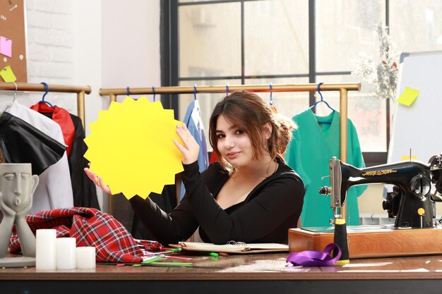 Linda senhora sentada no atelier e segurando o quadro de ideias enquanto olha para a câmera