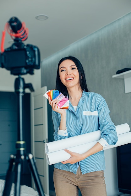 Linda senhora sorridente com plantas e amostras de paleta de cores gravando um vídeo e olhando para a câmera no tripé