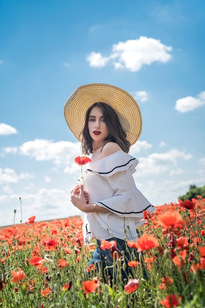 Linda senhora ucraniana sozinha com chapéu de palha no campo de papoulas de flores, dia sexy e ensolarado