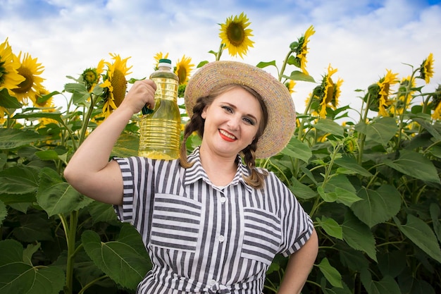 Linda sorridente alegre agricultora de meia idade segurando garrafas de óleo de girassol dourado nas mãos em um campo de colheita de girassóis em um dia ensolarado