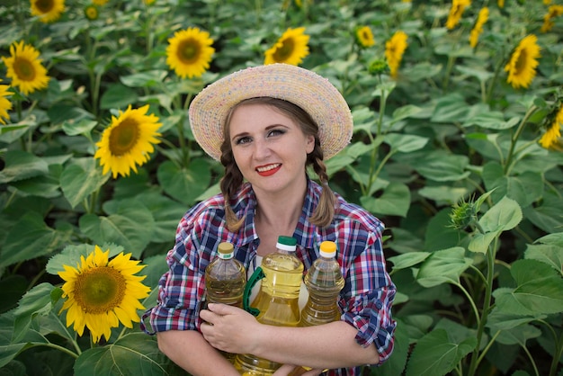 Linda sorridente alegre agricultora de meia idade segurando garrafas de óleo de girassol dourado nas mãos em um campo de colheita de girassóis em um dia ensolarado