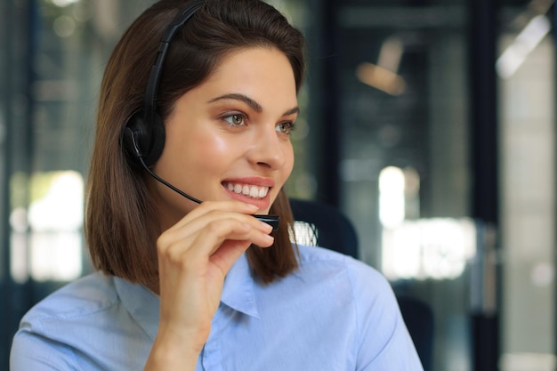 Linda sorridente trabalhadora de call center em fones de ouvido está trabalhando no escritório moderno