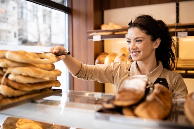 Linda sorridente trabalhadora de padaria vendendo pastelaria fresca para o cliente na padaria