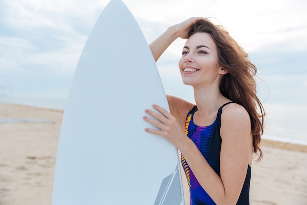 Linda surfista adolescente em pé com uma prancha de surf na praia