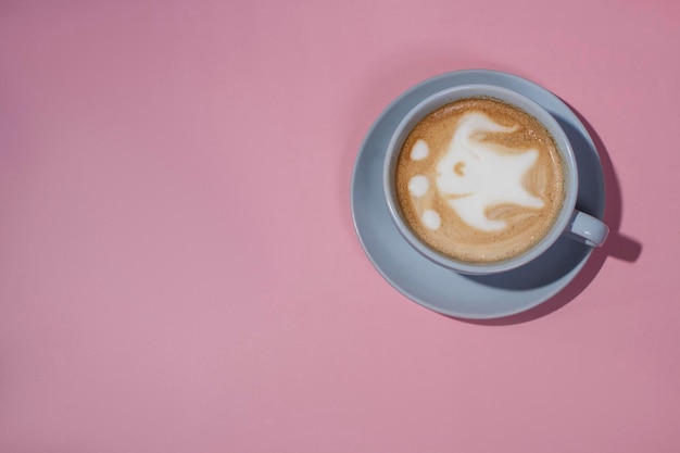 Linda taza de café de arte latte de pescado sobre fondo rosa