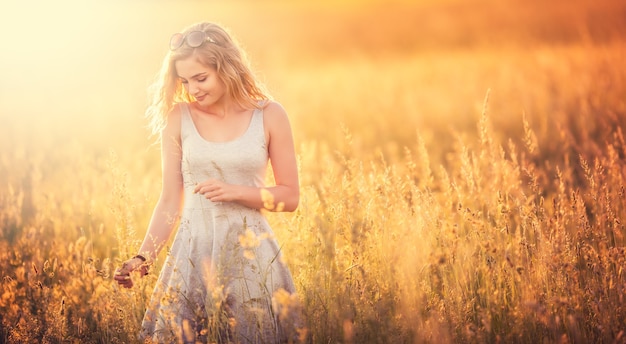 Linda tenra jovem loira em pé no prado de verão com vestido cinza. Mulher livre e feliz curtindo a natureza.