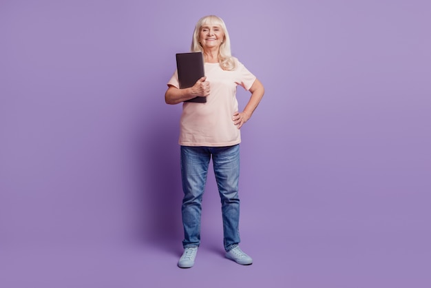 Linda velha gerente segurando laptop sobre fundo roxo
