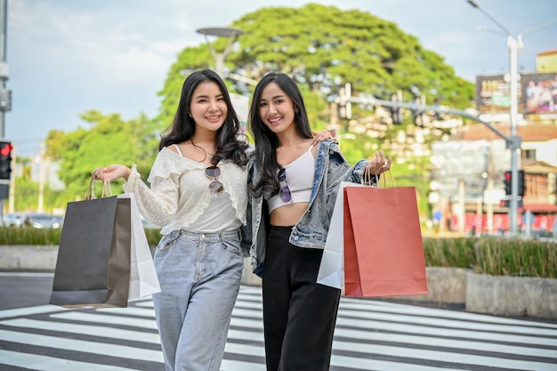 Lindas amigas asiáticas com suas sacolas de compras andando pela rua comercial