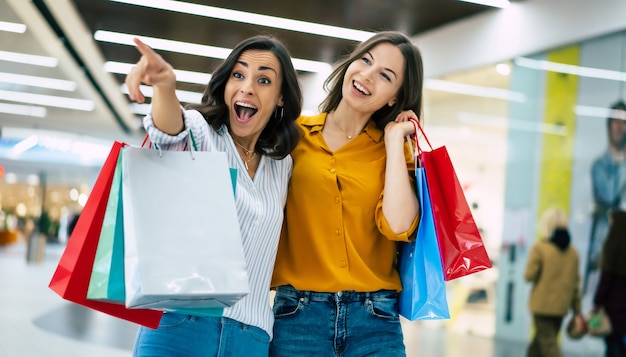 Lindas amigas felizes e animadas com sacos de papel andando pelo shopping