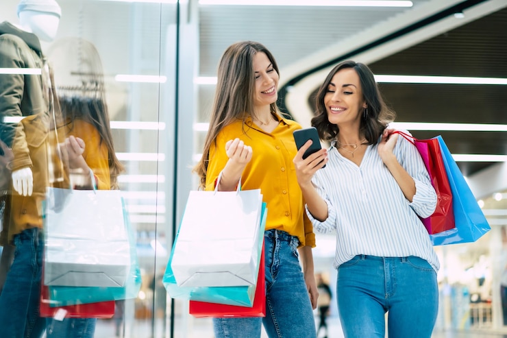 Foto lindas amigas felizes e animadas com sacos de papel e um telefone inteligente andando pelo shopping