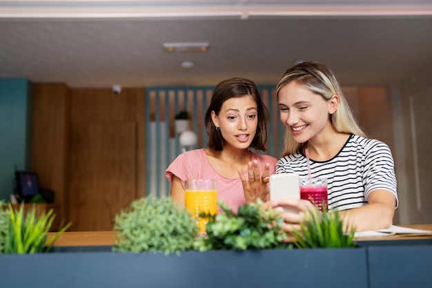 Lindas amigas jovens usando o telefone celular juntas e se divertindo