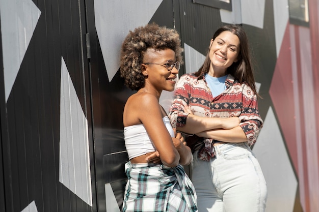 Lindas amigas negras e brancas estão encostadas em uma parede sorrindo