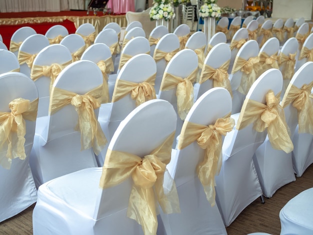 Lindas cadeiras de casamento brancas e limpas decoradas com fitas de ouro na cerimônia de casamento