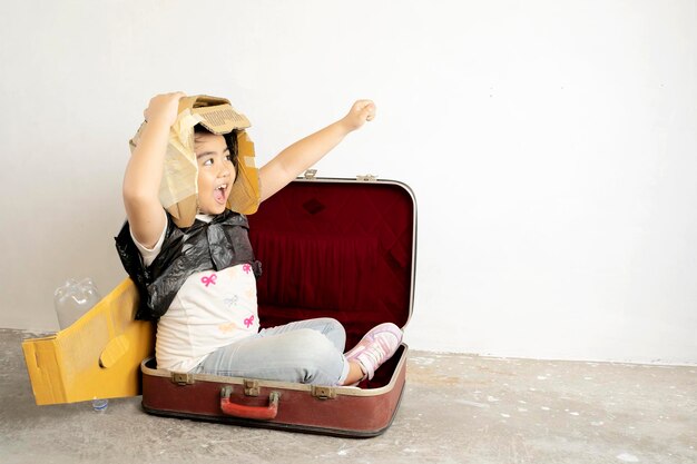 Lindas chicas asiáticas disfrutan jugando como se imaginan Viajan a su sueño sentándose en una maleta Hay un casco y alas de avión hechas de papel de caja con fondo blancoxA
