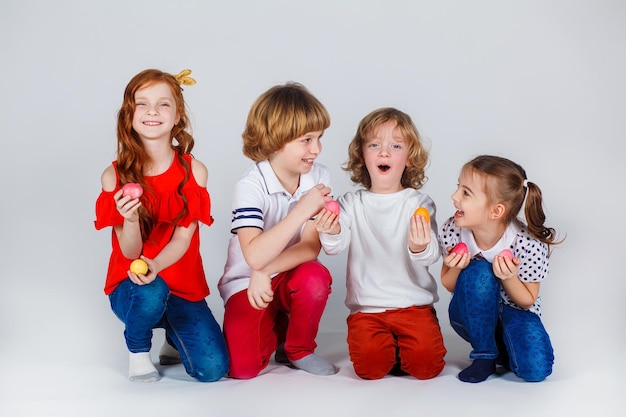 Foto lindas crianças em um fundo branco estão de pé com ovos de páscoa e se divertindo. momentos engraçados. conceito de férias de primavera. celebração da páscoa em família.