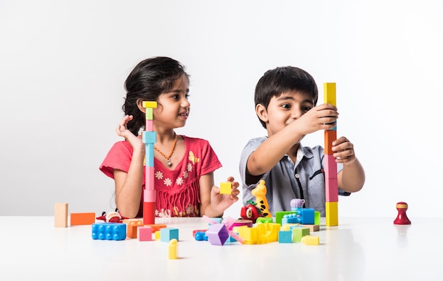 Lindas crianças indianas asiáticas brincando com brinquedos de plástico coloridos ou blocos enquanto estão sentadas à mesa ou isoladas sobre um fundo branco