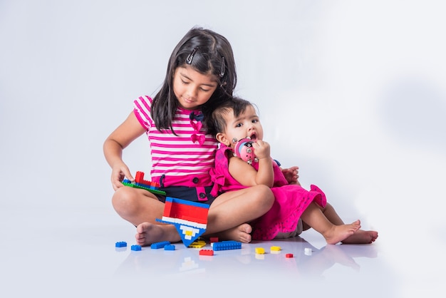 Lindas crianças indianas ou asiáticas brincando com brinquedos ou blocos e se divertindo enquanto estão sentadas à mesa ou isoladas sobre um fundo branco