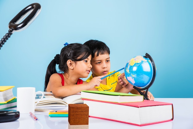 Lindas crianças indianas ou asiáticas estudando na mesa de estudo com uma pilha de livros, globo educacional, isolado sobre a cor azul claro